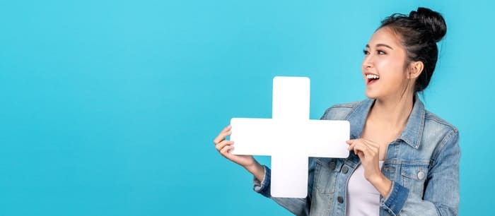 Jeune femme souriante tenant un grand signe plus